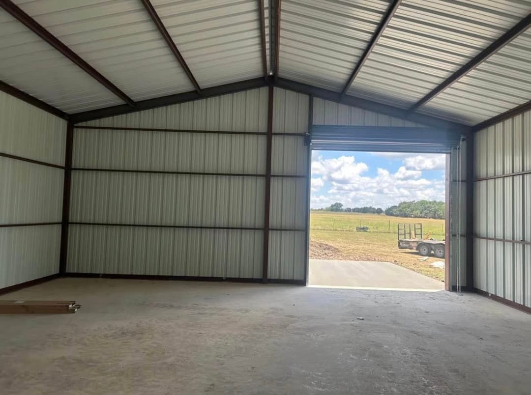Spacious metal warehouse interior with open door, grassy field visible outside.