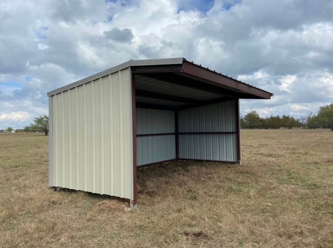 Steel shelter for animals in a grassy field under a cloudy sky. Suitable for outdoor use.
