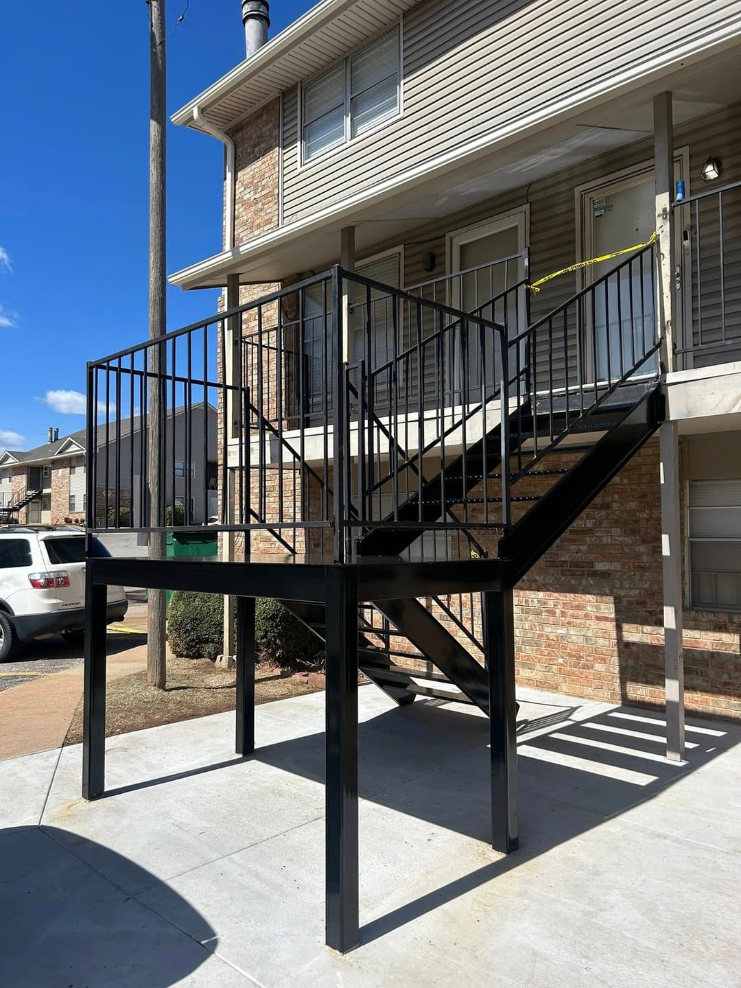Black metal staircase with railing leading to an apartment entrance, sunny outdoor setting.