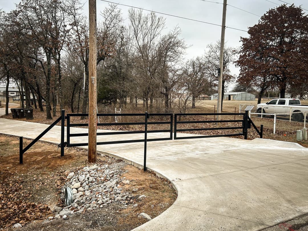 Black metal railing along a curved concrete driveway amidst fall foliage in a rural setting.
