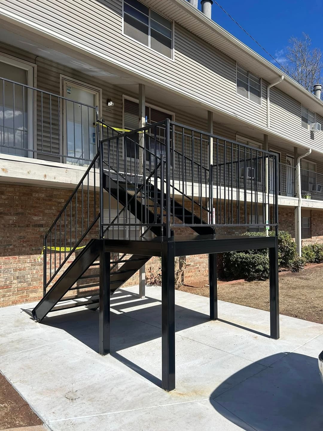 Black metal staircase for apartment building with safety railings and concrete landing.