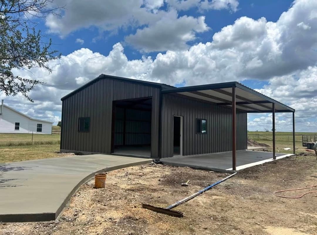 Metal building with a covered porch, concrete pathway, and blue sky with clouds.